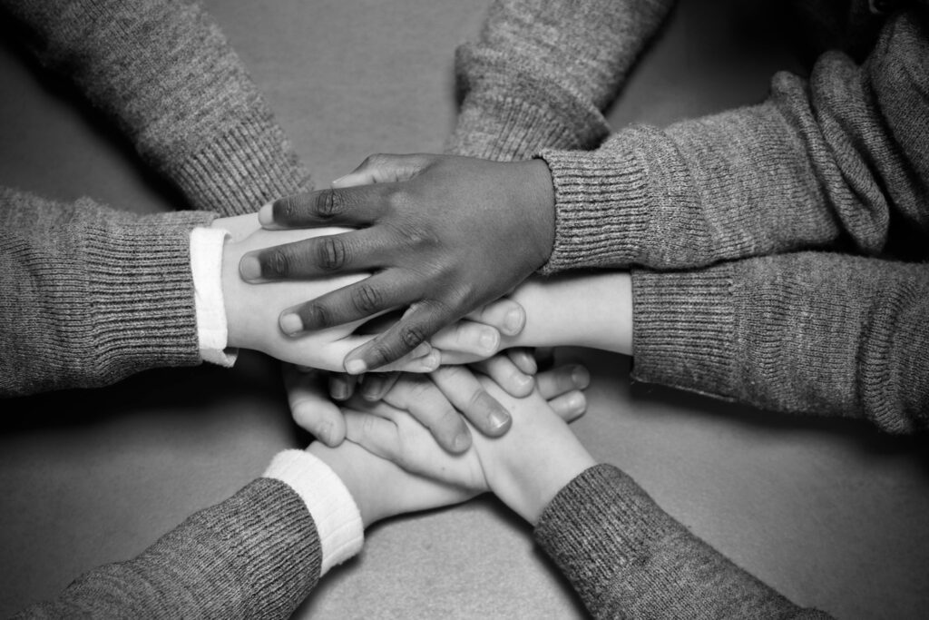 Black and white image of children's hands huddled together symbolizing unity and friendship.