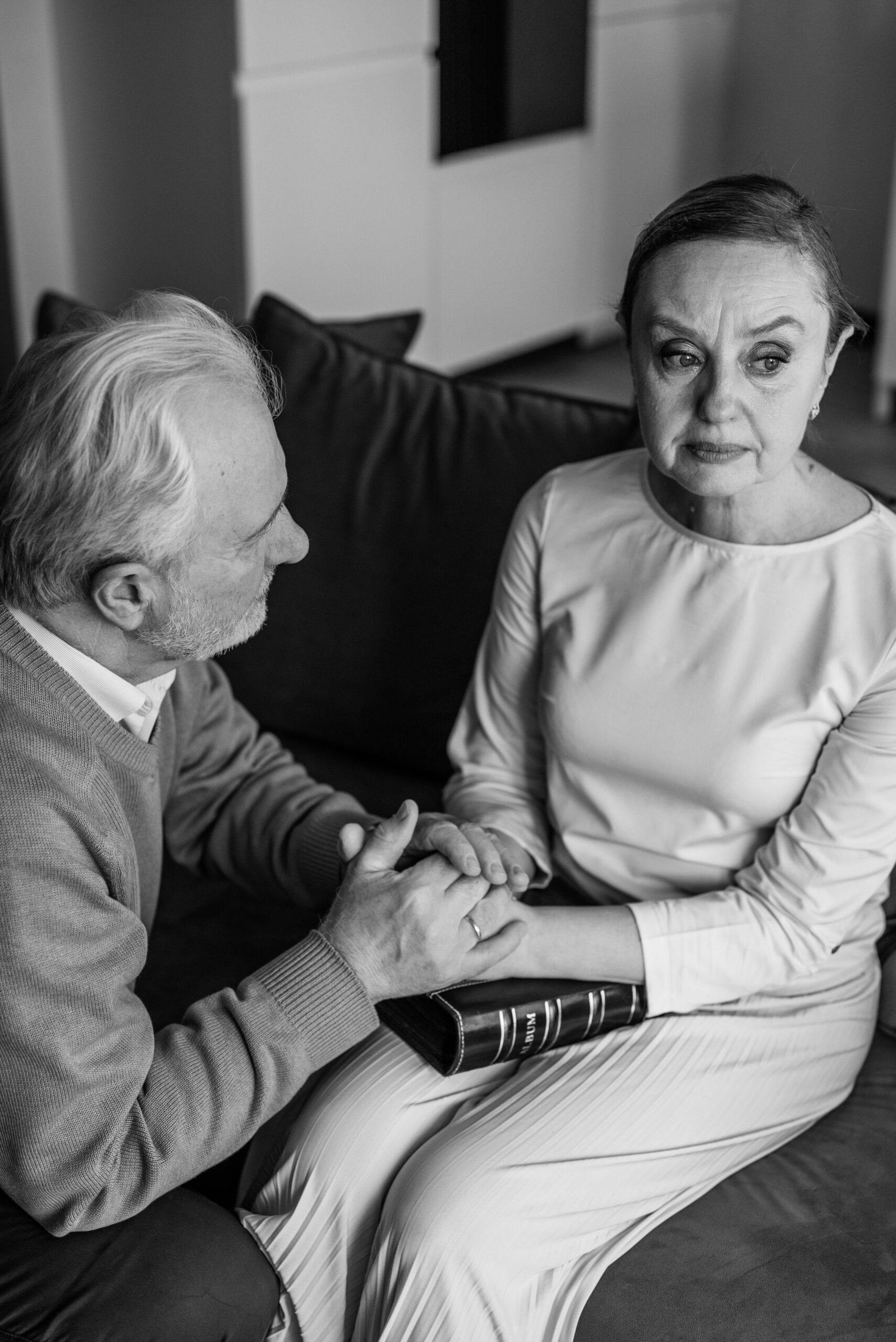 Black and white image of an elderly couple sitting together, sharing a moment of grief and support.