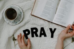 Bible open beside coffee cup with 'PRAY' letters on fabric, depicting peaceful study.